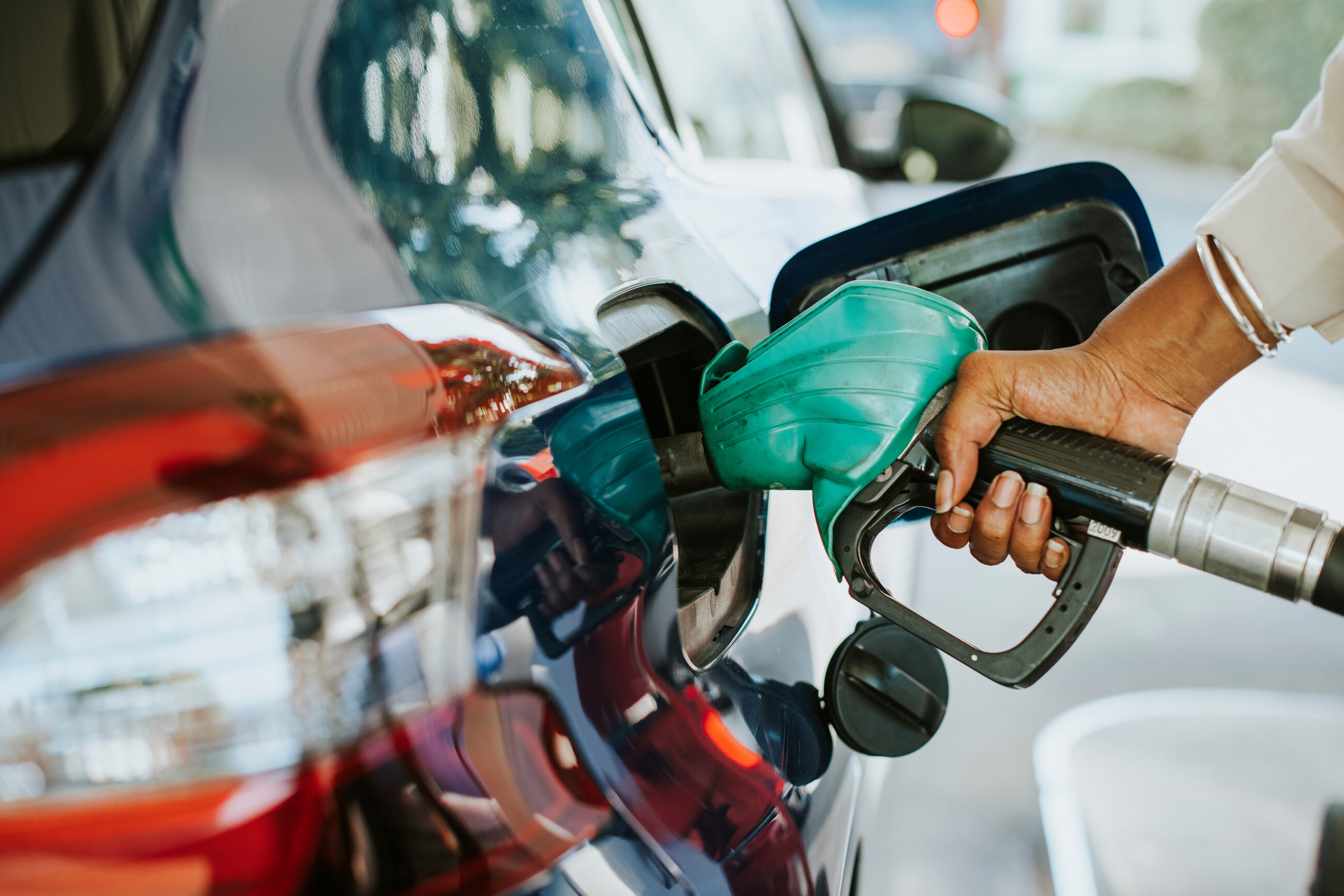 Main insérant un pistolet de distribution de carburant dans le réservoir d'une voiture rouge